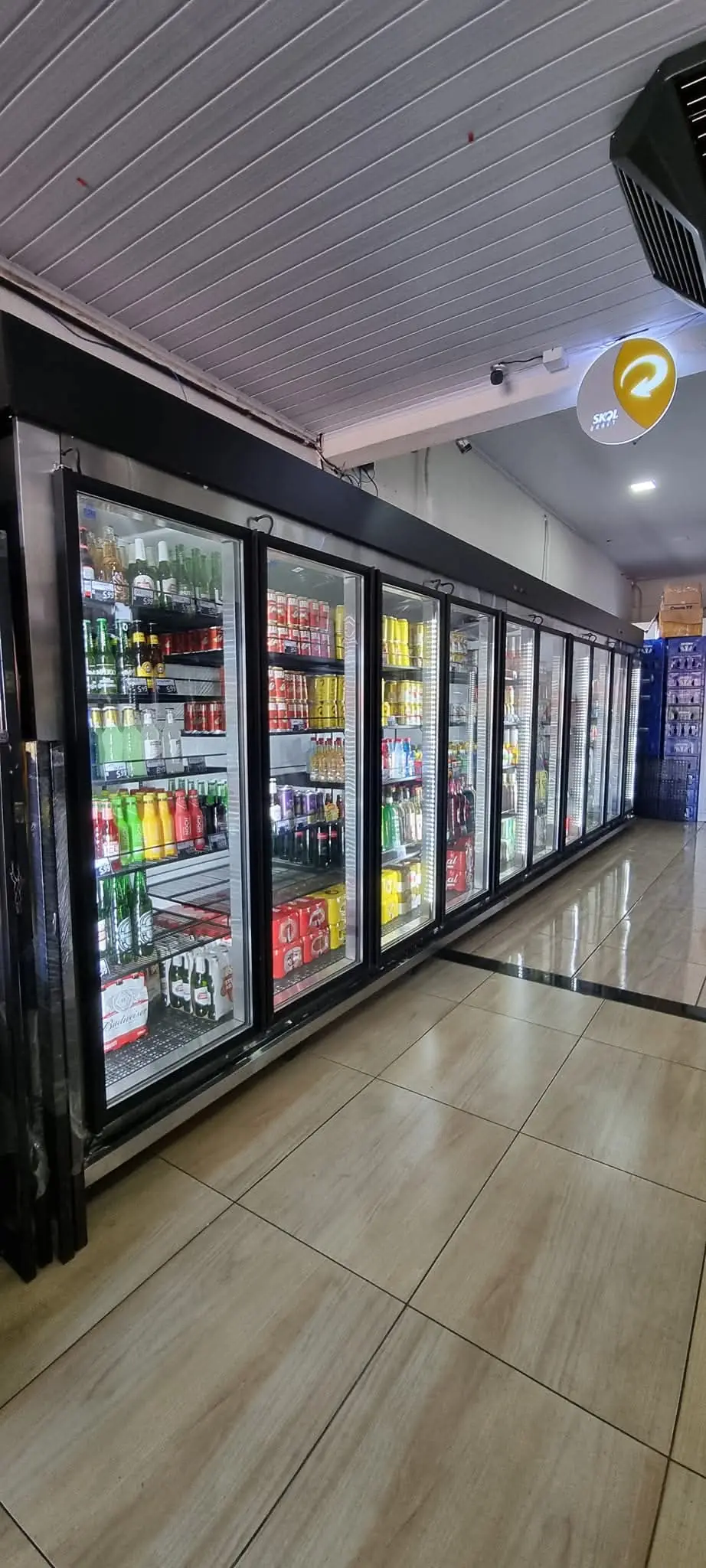 Câmara fria expositora com portas de vidro e prateleiras cheias de bebidas em mercado